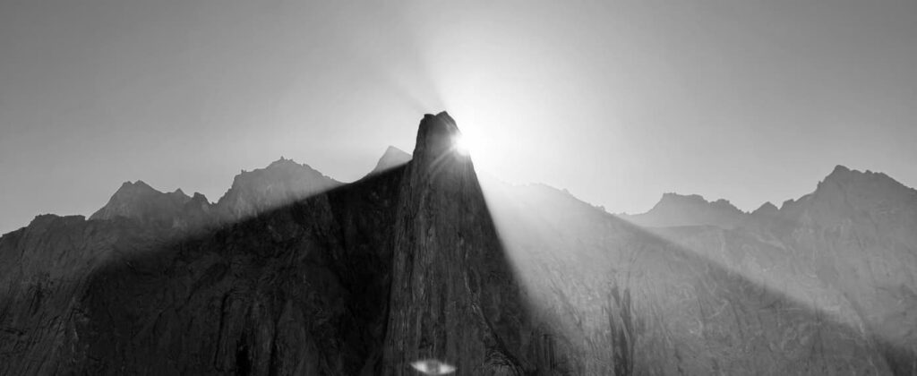Die Sonne geht hinter einem zerklüfteten Berggipfel auf und taucht eine schroffe Bergkette in Schwarz-Weiß in dramatisches Licht – eine atemberaubende Szenerie, die oft von staatlich geprüften Bergführern erkundet wird, die Abenteurer sicher durch diese majestätischen Landschaften führen.