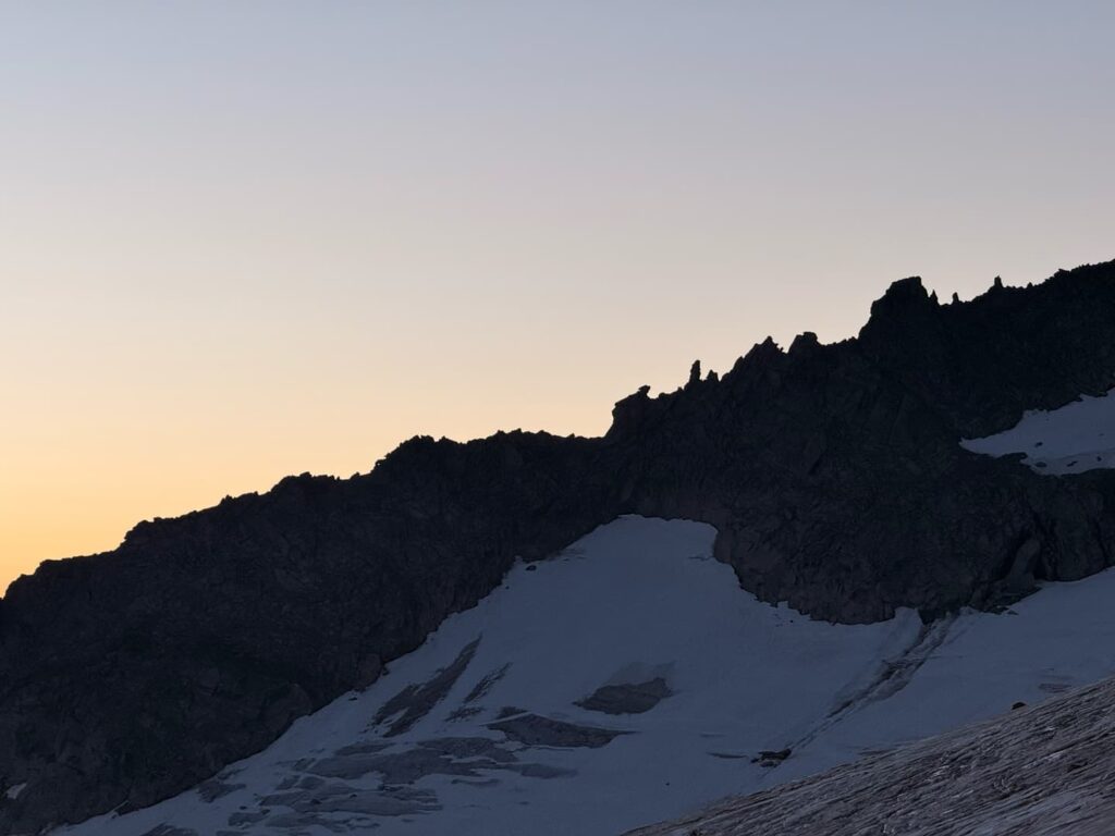 Ein Gebirgskamm mit schroffen Gipfeln, die sich gegen den Abendhimmel abzeichnen, und Schneeflecken, die die felsigen Hänge im Vordergrund bedecken – eine atemberaubende Szenerie, die an ein Abenteuer bei einer Skitour auf den Großvenediger erinnert.
