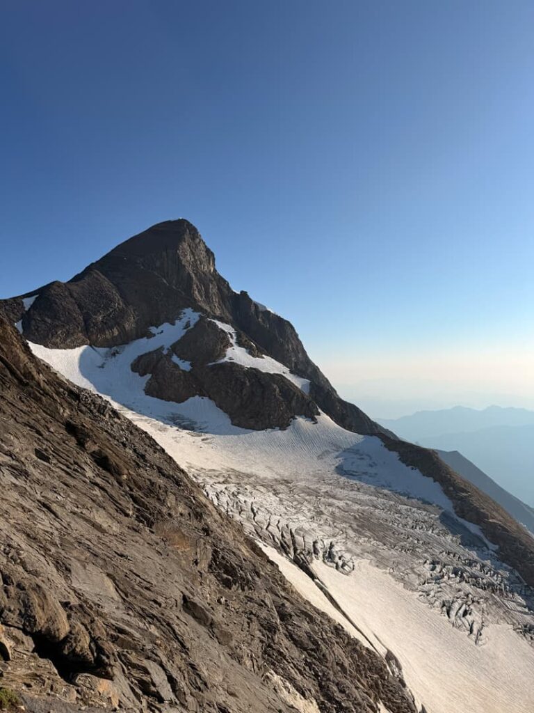 Ein felsiger Berggipfel, wie das Große Wiesbachhorn, ragt unter strahlend blauem Himmel über einen Gletscher empor, während das Sonnenlicht Schatten auf die Schnee- und Felshänge wirft.