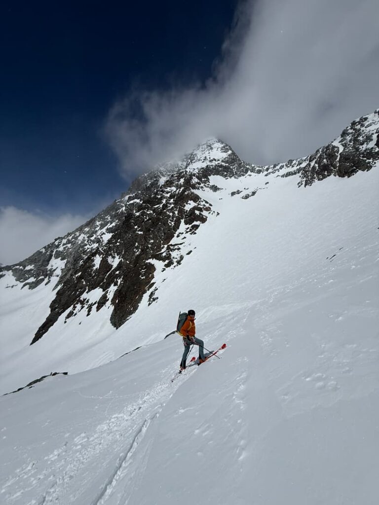 Eine Person mit Rucksack steht auf Skiern im Tiefschnee und blickt unter einem teilweise bewölkten Himmel auf einen verschneiten Berghang – bereit, sich auf ein Abenteuer bei der „Skitour Großglockner geführt“ zu begeben.