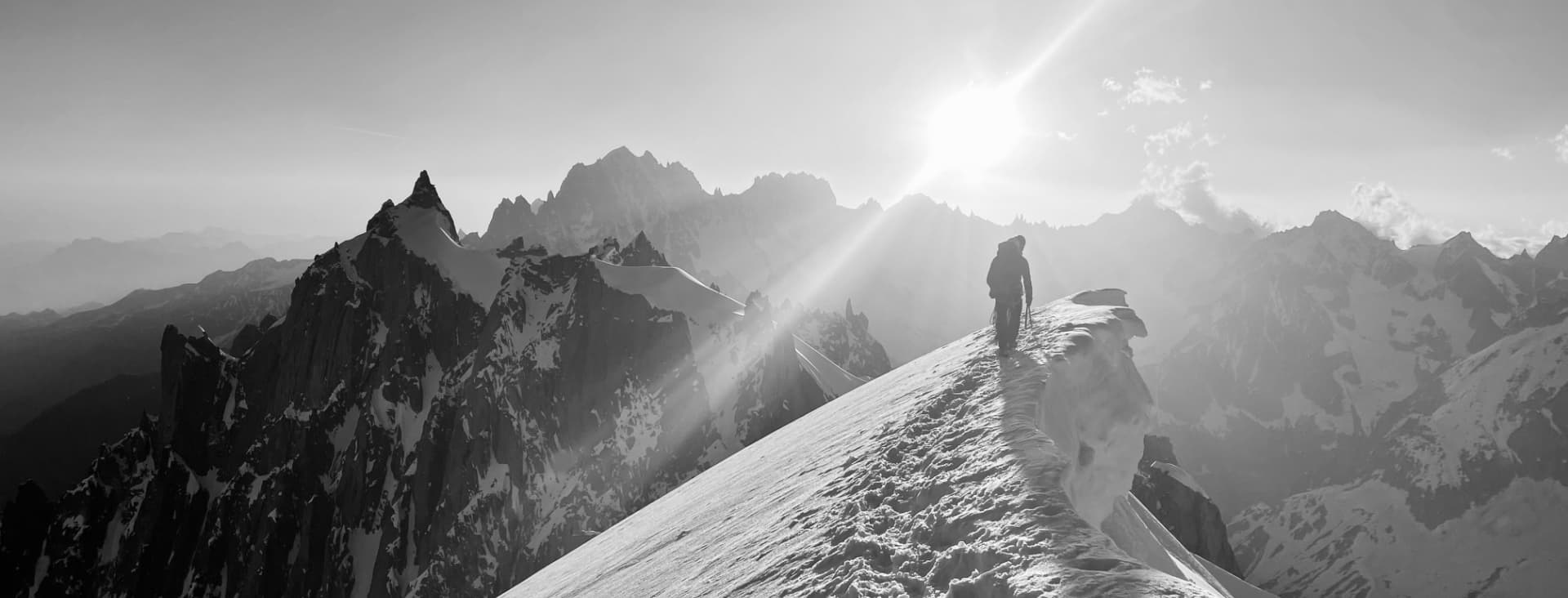 Eine Person wandert entlang eines verschneiten Bergrückens, im Hintergrund ragen schroffe Gipfel empor, während die Sonne hell am Himmel strahlt – ein typischer „ARE YOU SUMMIT“-Moment, in dem Abenteuer und Gelassenheit verschmelzen. Für weitere Informationen wenden Sie sich bitte über „Kontakt“ an uns.