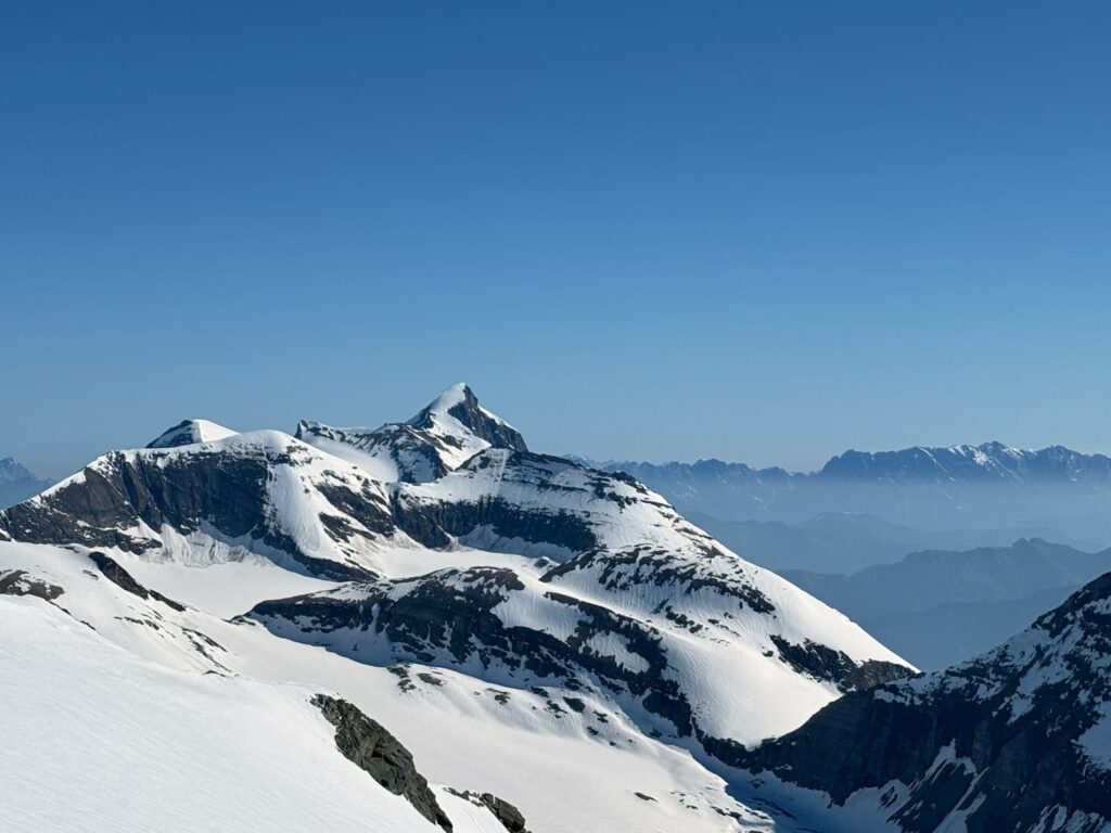 Schneebedeckte Berggipfel unter strahlend blauem Himmel, mit schroffen Bergrücken und in der Ferne im Dunst liegenden Bergen im Hintergrund – ein atemberaubender Anblick, perfekt für ein „3000er Salzburger Land geführt“-Abenteuer.