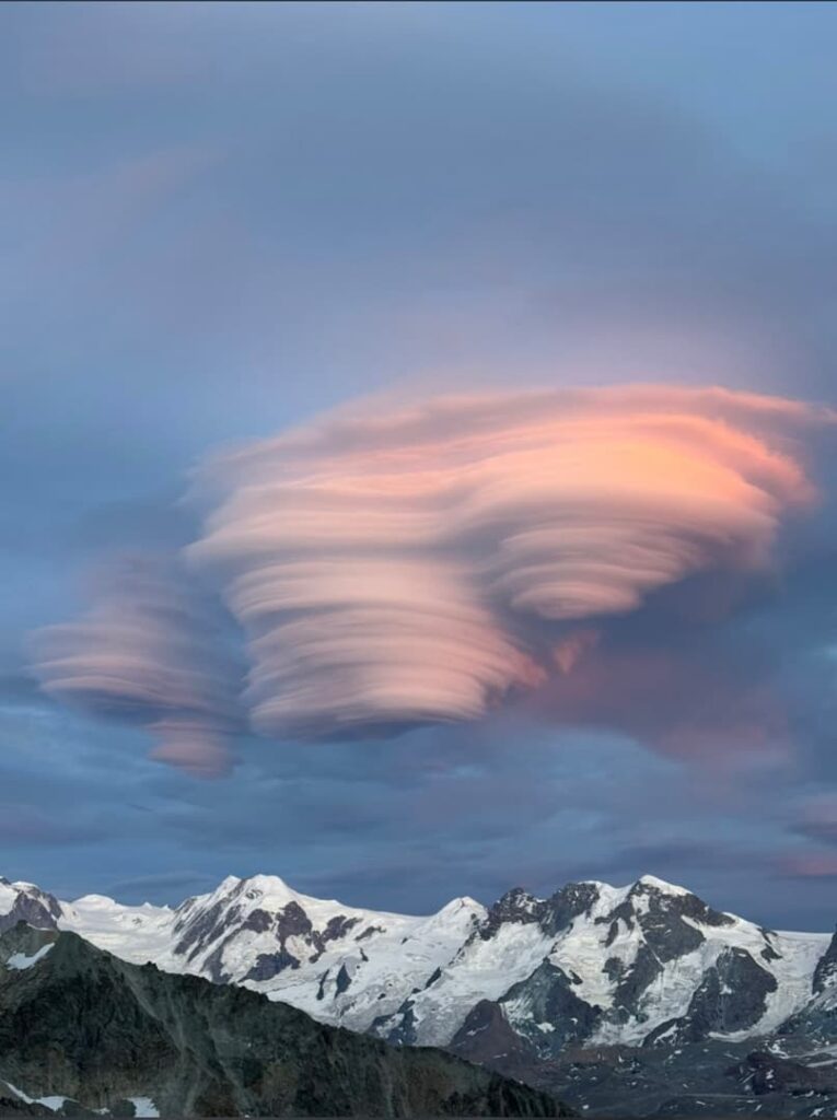 In der Abenddämmerung schweben linsenförmige Wolken mit rosa Schimmer über den schneebedeckten Berggipfeln und schaffen so ein dramatisches und surreal anmutendes Himmelsbild – ein atemberaubender Anblick, den man oft bei einer Führung auf den Lyskamm bewundern kann.
