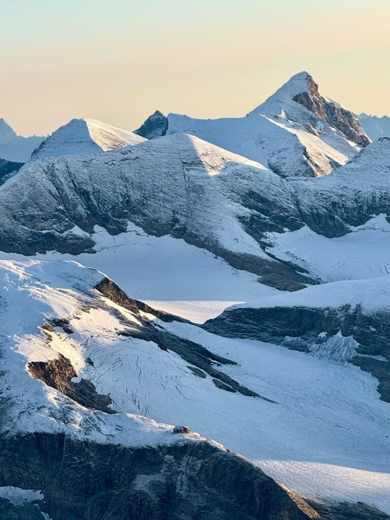 Die schneebedeckten 3000er-Gipfel des Salzburger Landes unter klarem Himmel, während das Sonnenlicht Schatten auf die Hänge wirft und sich zwischen den Bergrücken ein Gletscher schmiegt – ein unvergessliches, geführtes Alpenerlebnis.
