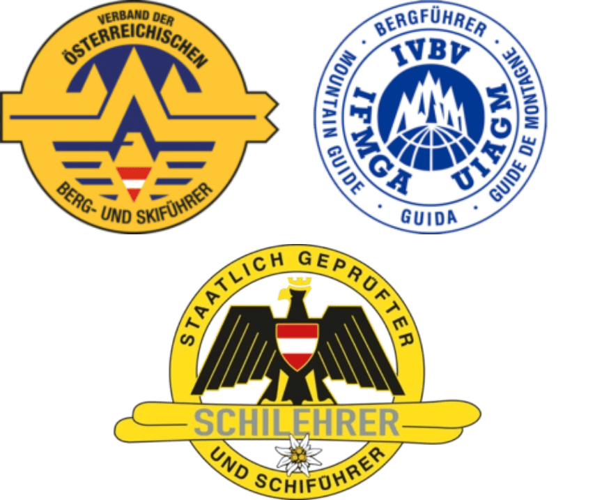 Drei runde Abzeichen: ein gelbes österreichisches Bergführerlogo, ein blaues internationales Bergführeremblem und ein gelbes Abzeichen mit einem schwarzen Adler und der Aufschrift „Schilehrer“, die auf zertifizierte Skilehrer und staatlich geprüfte Bergführer hinweisen.