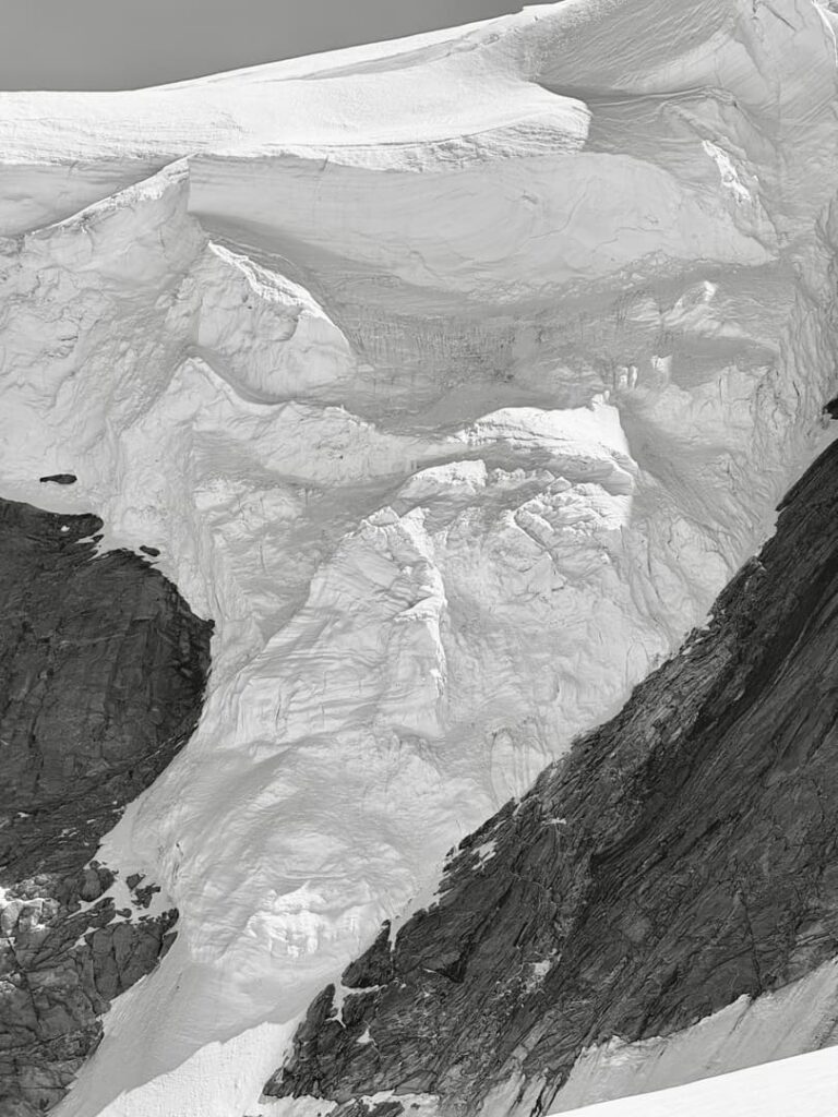 Eine Nahaufnahme eines Gletschers an einem Berghang, die Schichten aus Schnee und Eis mit zerklüfteten Strukturen neben dunklem, freiliegendem Gestein zeigt – eine beeindruckende Szenerie, die man auf geführten Bergtouren in den Alpen oft zu sehen bekommt.